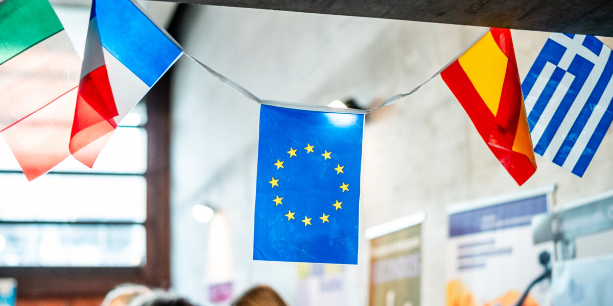 Miniaturflaggen von Italien, Frankreich, Spanien, Griechenland und der EU hängen als Wimpelkette an einem Infostand