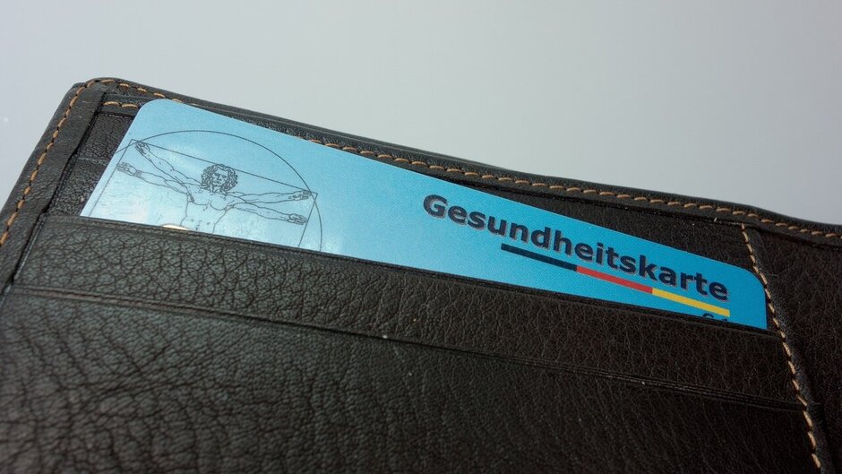 Man sieht eine aufgefaltete Geldbörse. Im obersten Fach befindet sich eine blaue Gesundheitskarte. 
