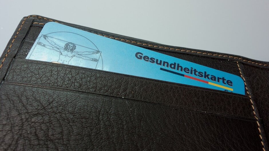 Man sieht eine aufgefaltete Geldbörse. Im obersten Fach befindet sich eine blaue Gesundheitskarte. 