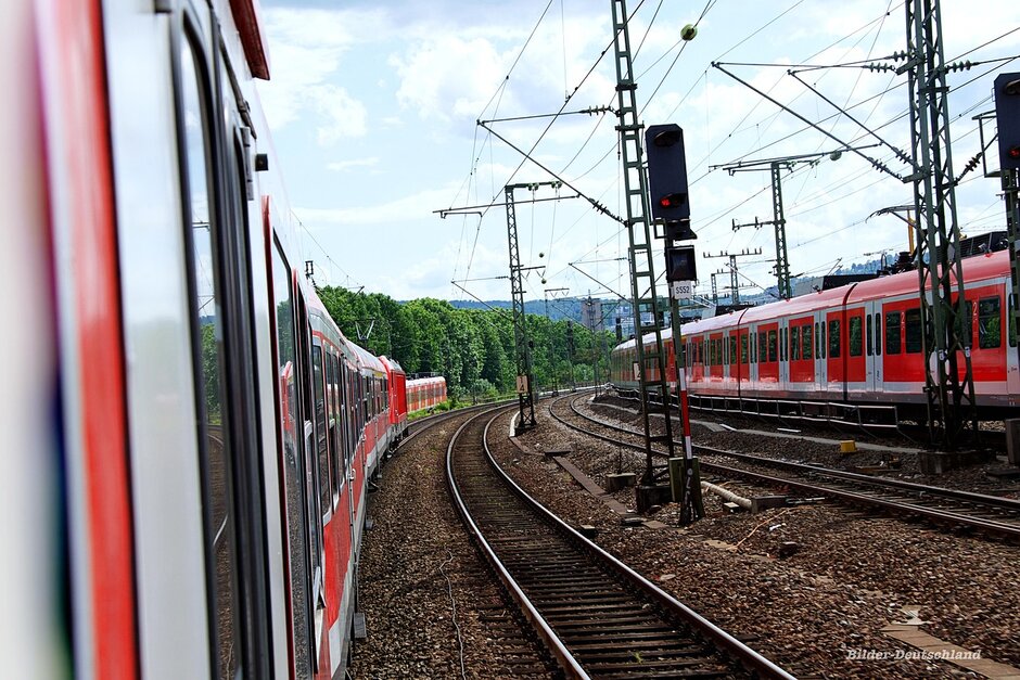 Man sieht zwei rote Regionalzüge auf Bahngleisen fahren. 
