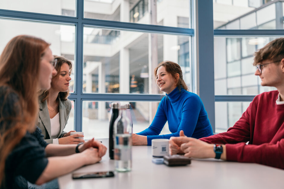 Drei Studentinnen und Studenten sitzen bei einer gemeinsamen Pause an einem Tisch.