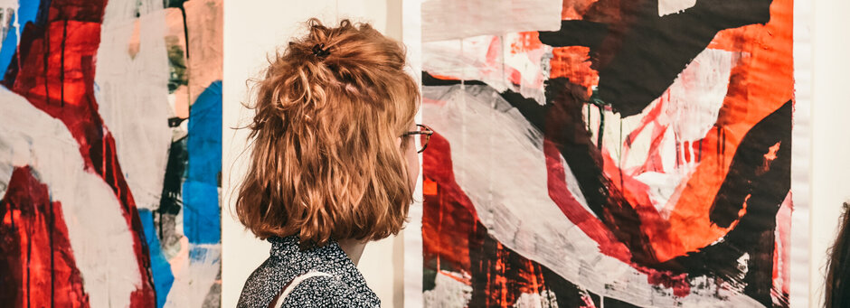 Junge Frauen betrachten abstrakte Kunstwerke bei einer Ausstellungseröffnung.