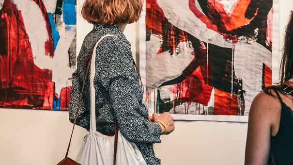 Junge Frauen betrachten abstrakte Kunstwerke bei einer Ausstellungseröffnung.