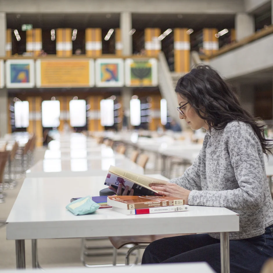 Eine junge Frau sitzt mit Büchern und Studienunterlagen an einem Tisch im Lesesaal "Philosophicum" an der Universität Regensburg.