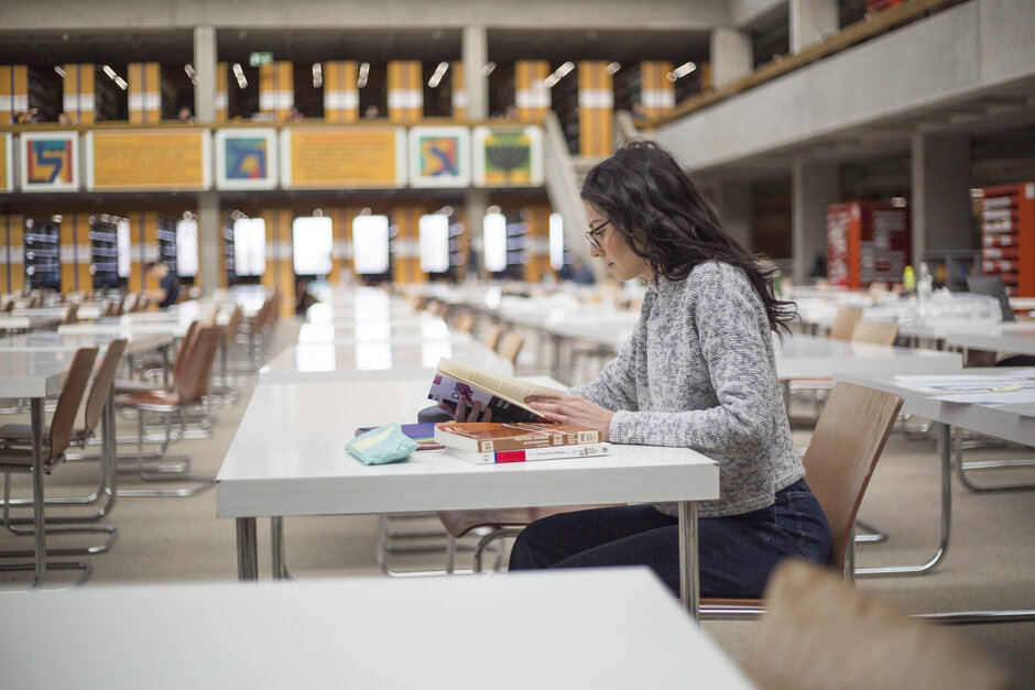 Eine junge Frau sitzt mit Büchern und Studienunterlagen an einem Tisch im Lesesaal "Philosophicum" an der Universität Regensburg.