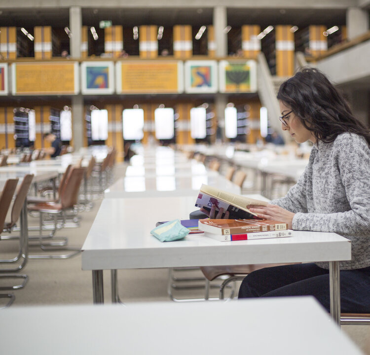 Eine junge Frau sitzt mit Büchern und Studienunterlagen an einem Tisch im Lesesaal "Philosophicum" an der Universität Regensburg.