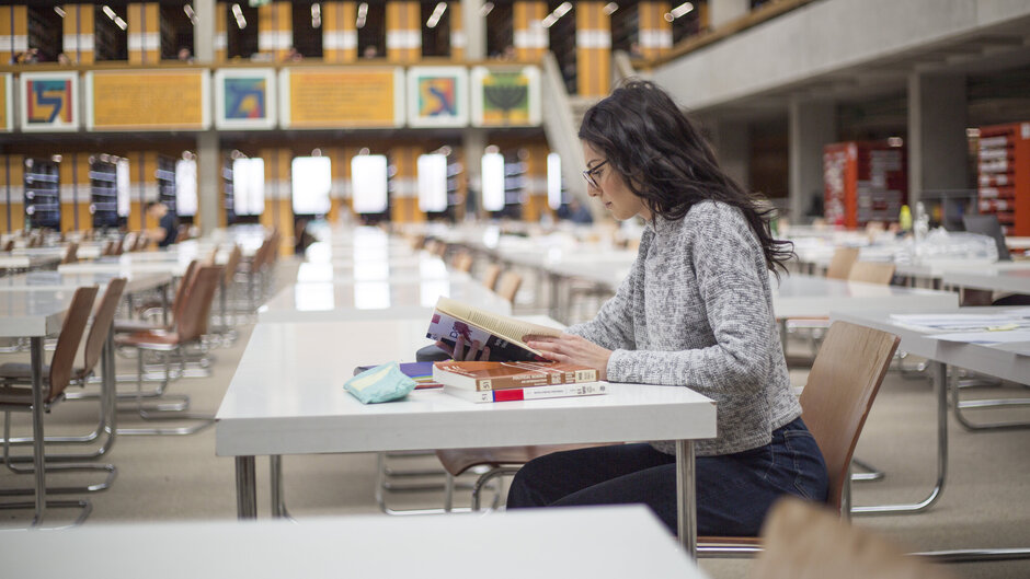 Eine junge Frau sitzt mit Büchern und Studienunterlagen an einem Tisch im Lesesaal "Philosophicum" an der Universität Regensburg.