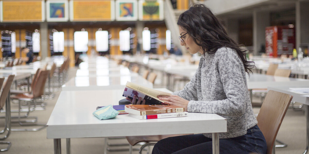 Eine junge Frau sitzt mit Büchern und Studienunterlagen an einem Tisch im Lesesaal "Philosophicum" an der Universität Regensburg.