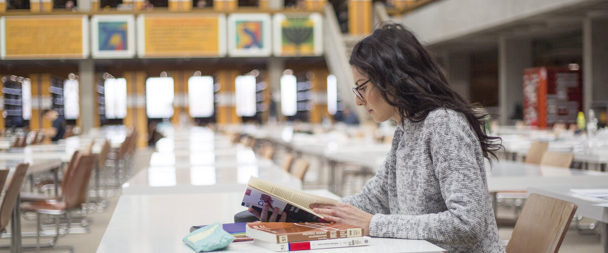 Eine junge Frau sitzt mit Büchern und Studienunterlagen an einem Tisch im Lesesaal "Philosophicum" an der Universität Regensburg.