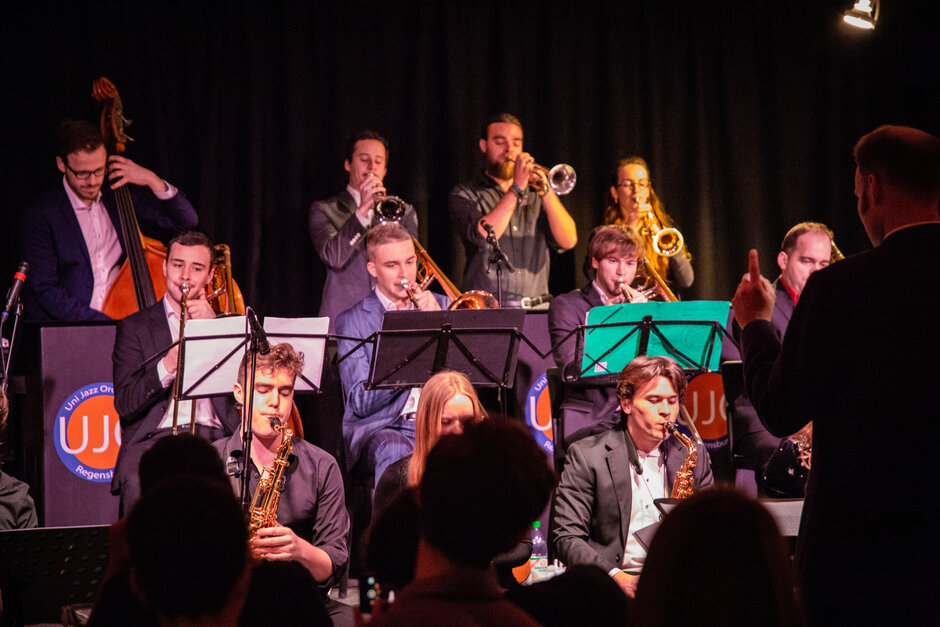 Eine Gruppe von jungen Menschen mit Musikinstrumenten musiziert. Im Vordergrund ist ein Dirigent zu erkennen. (öffnet Vergrößerung des Bildes)