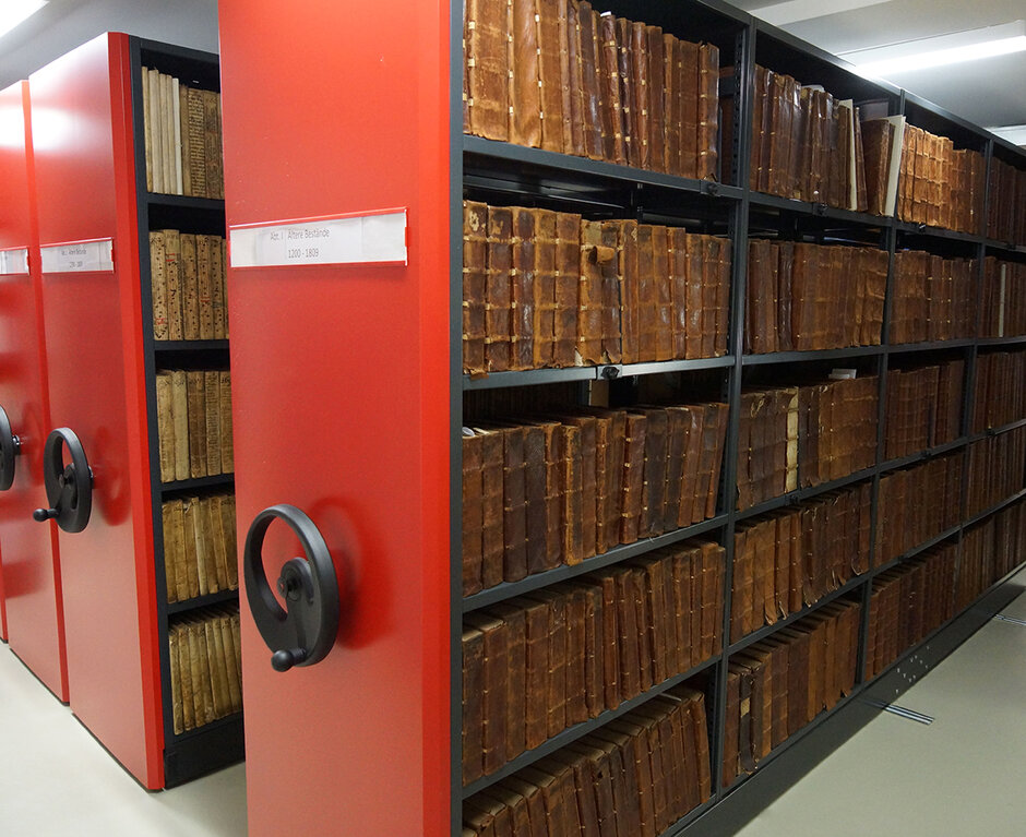 Archivraum mit verschiebbaren Regalen, gefüllt mit Reihen alter, braun gebundener Bücher. (öffnet Vergrößerung des Bildes)