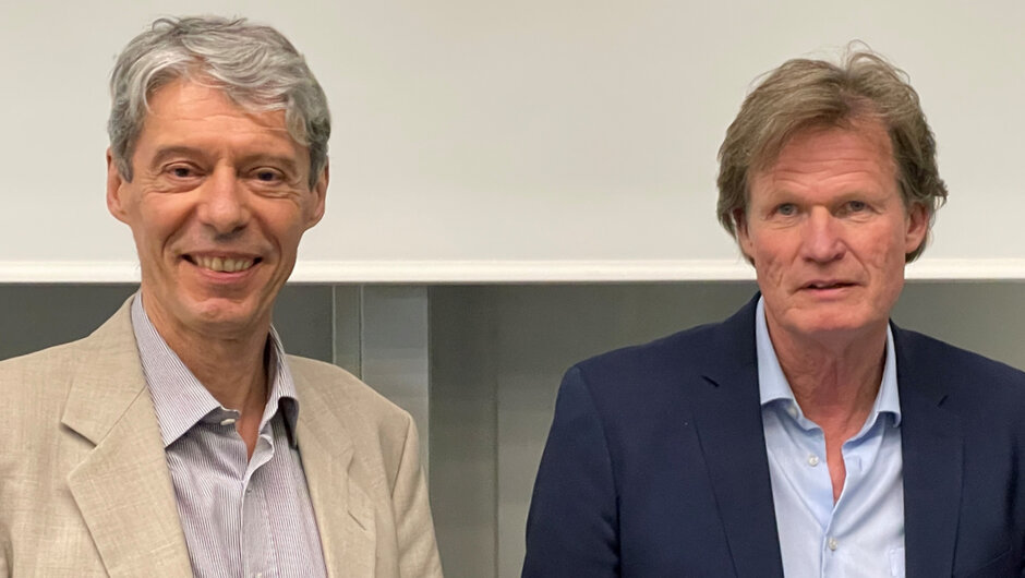 Zwei Männer stehend nebeneinander und blicken lächelnd in die Kamera.