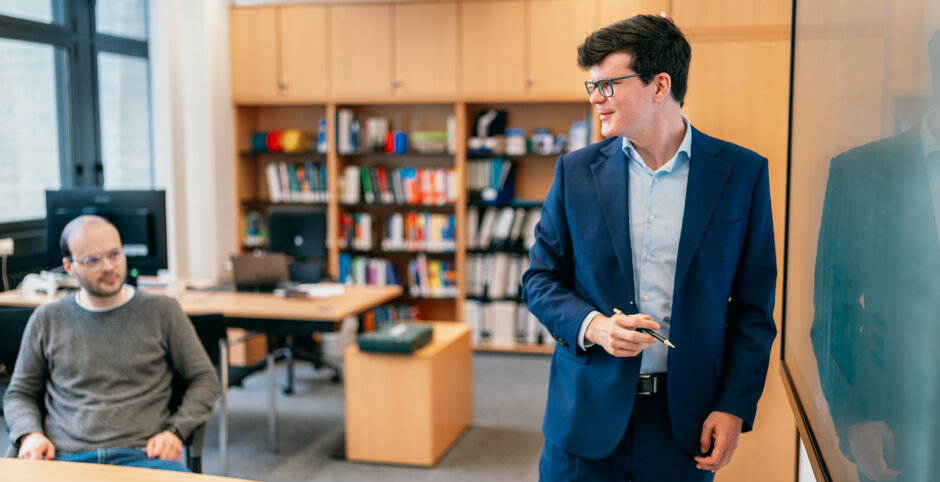 Ein Professor steht an einer elektronischen Tafel und erklärt seinen Zuhörern einen Sachverhalt.