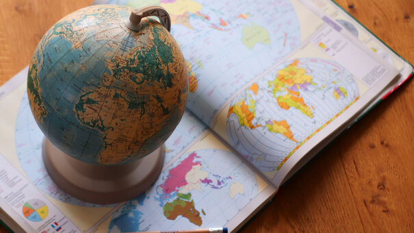 Ein Atlas liegt geöffnet auf dem Boden. Darauf steht ein Globus.