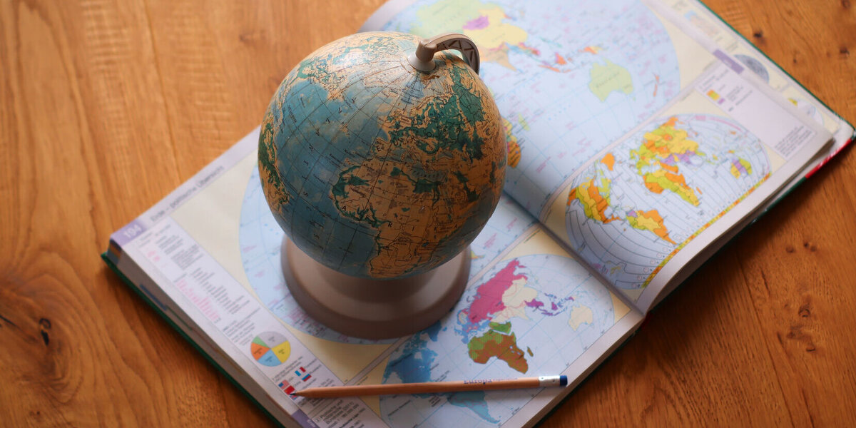 Ein Atlas liegt geöffnet auf dem Boden. Darauf steht ein Globus.