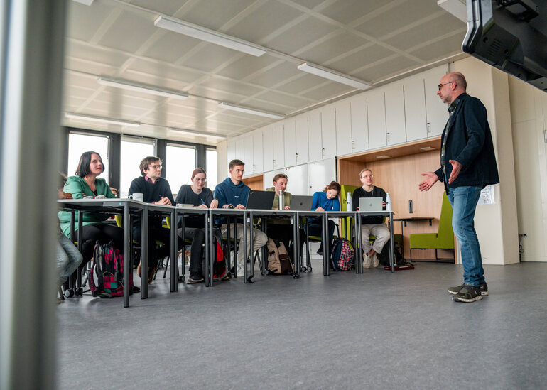 Ein Dozent hält einen Vortrag vor einer Gruppe von Studierenden in einem modern ausgestatteten Seminarraum an der Universität Regensburg
