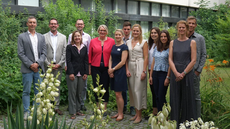 Ein Gruppenbild mit 12 Personen in einem gartenähnlichen Innenhof. (öffnet Vergrößerung des Bildes)