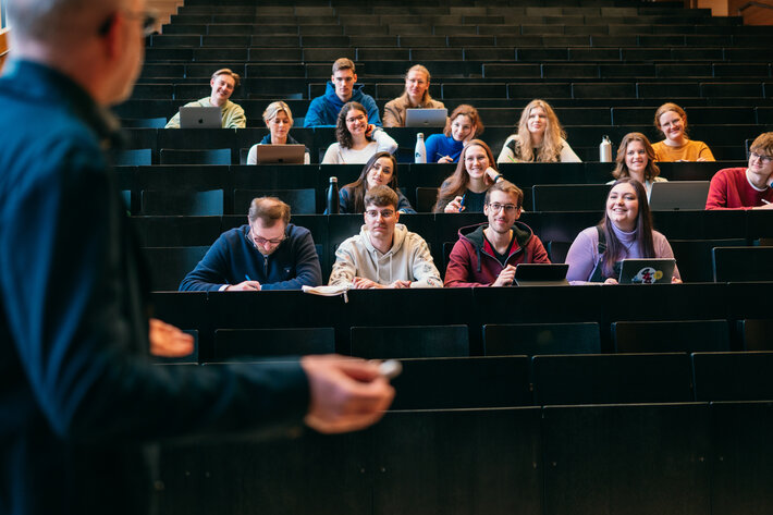 Ein Dozent spricht in einem Hörsaal zu Studierenden. (öffnet Vergrößerung des Bildes)