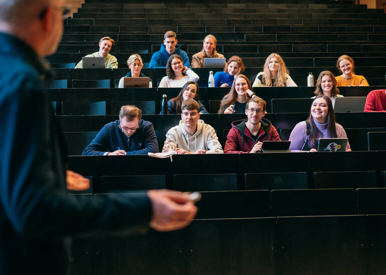 Ein Dozent spricht in einem Hörsaal zu Studierenden.