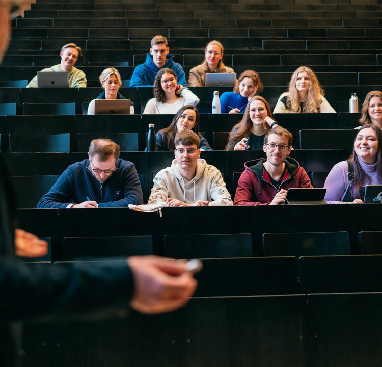 Ein Dozent spricht in einem Hörsaal zu Studierenden.