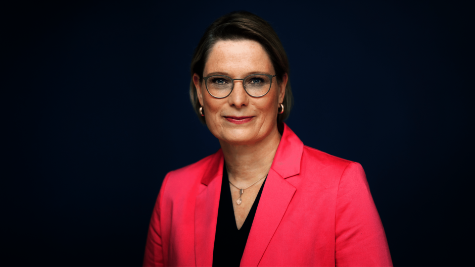 Frau in rosa Jackett schaut direkt in die Kamera.