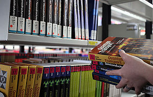 Hand hält einen Stapel Bücher vor einem Buchregal
