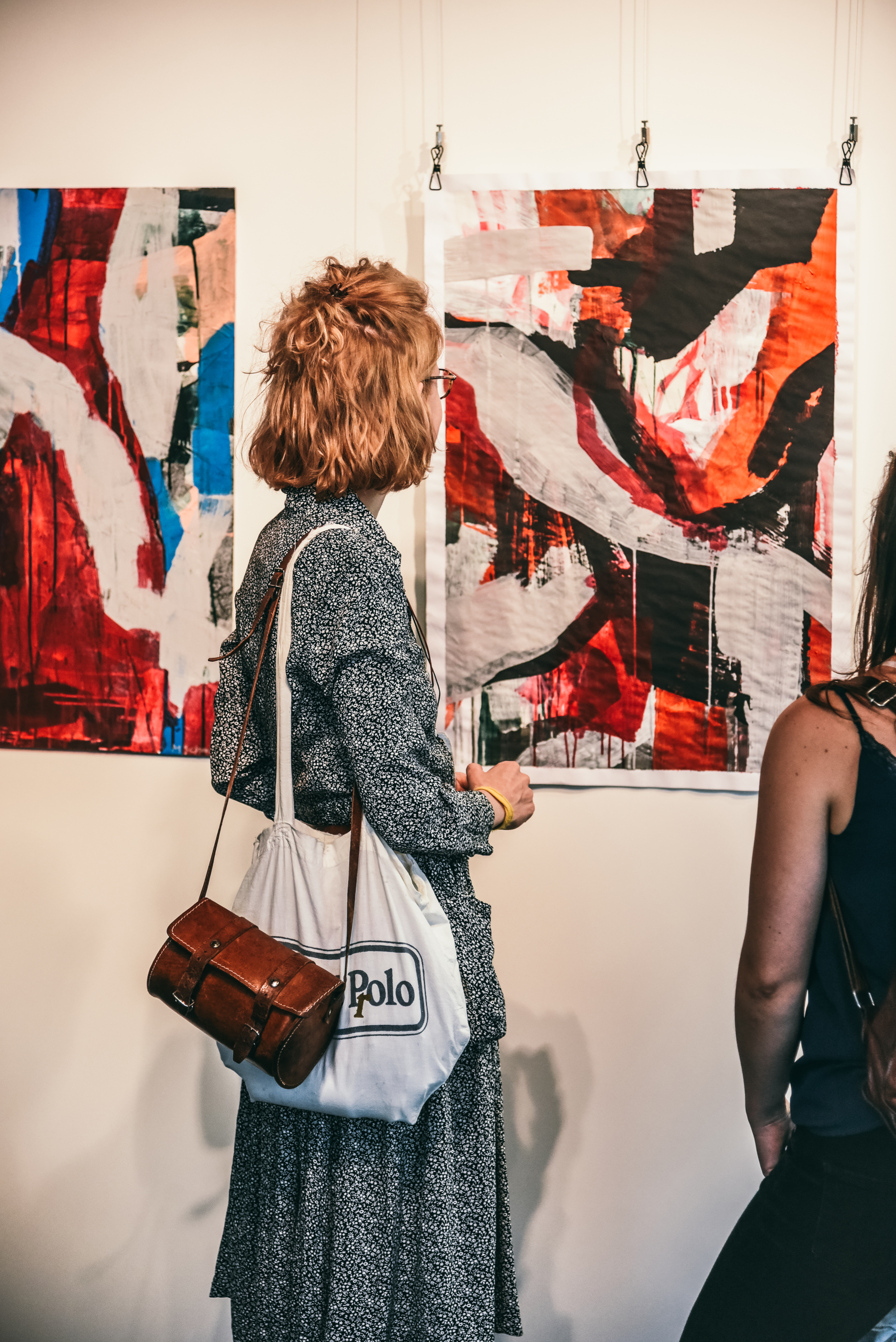 Junge Frauen betrachten abstrakte Kunstwerke bei einer Ausstellungseröffnung.