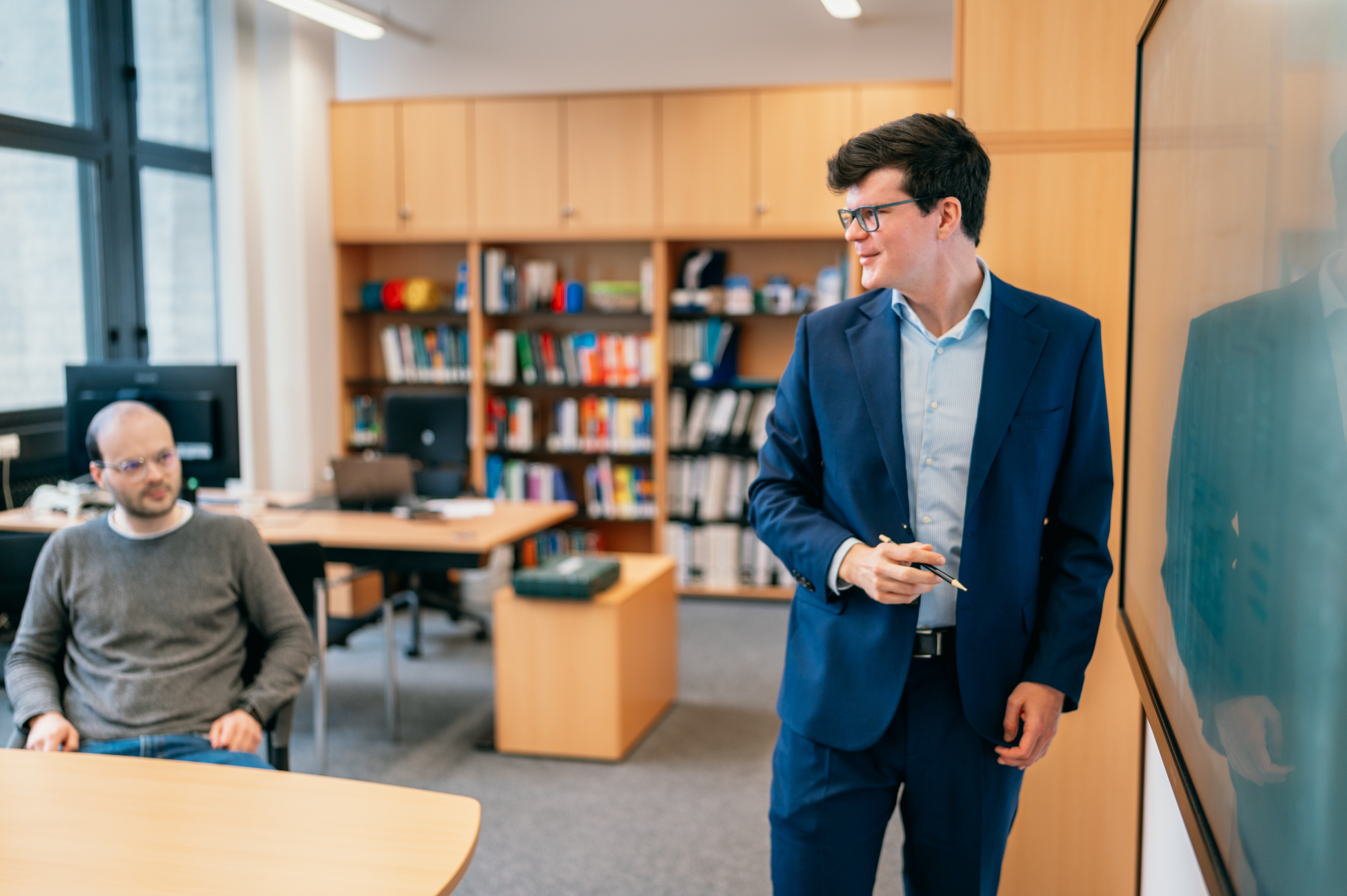 Ein Professor steht an einer elektronischen Tafel und erklärt seinen Zuhörern einen Sachverhalt.