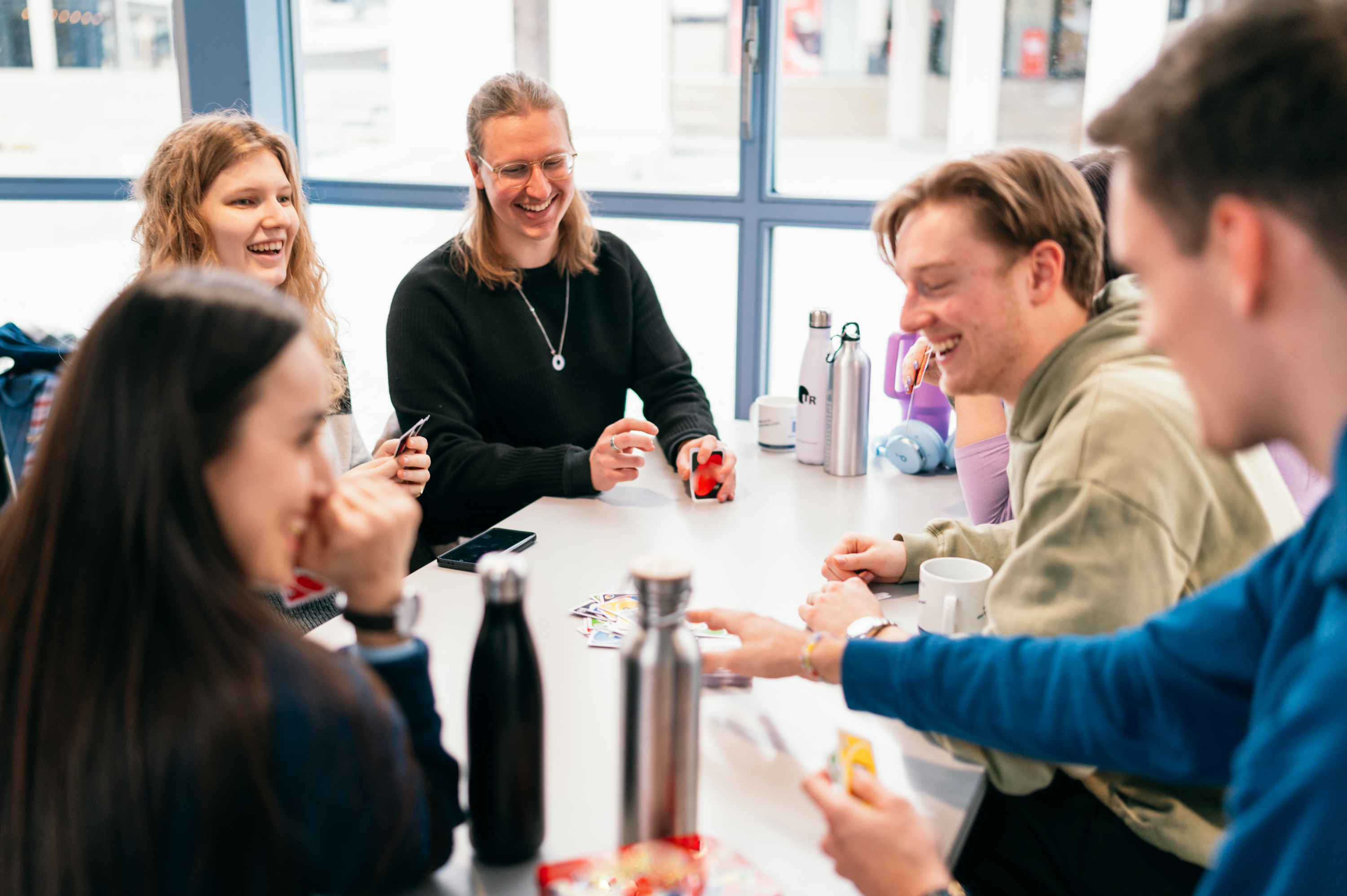 Eine Gruppe Studierender spielt Karten an einem Tisch in einer Cafeteria.