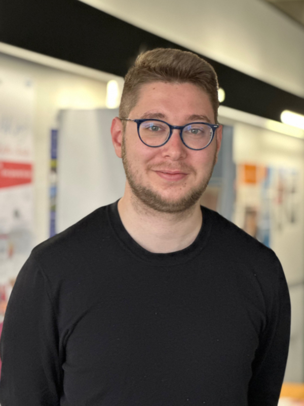 Ein jüngerer Mann mit Brille, Bart und schwarzem Pullover blickt mit freundlichem Gesichtsausdruch in die Kamera.