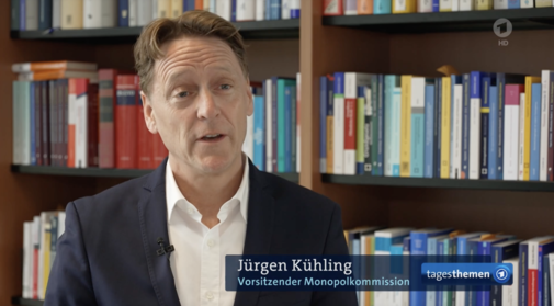 Ein Mann mit weißem Hemd und Anzugjacke sitzt vor einem Bücherregal und spricht. Seine Augenbrauen sind nach oben gezogen, seine Stirn ist in Falten gelegt. Am rechten unteren Bildrand ist das Logo der "tagesthemen" und der ARD eingeblendet. Daneben steht "Jürgen Kühling | Vorsitzender Monopolkommission".