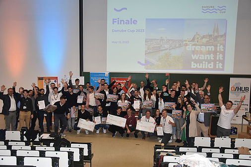 Gruppenfoto mit mehreren Personen; viele von ihnen halten in Jubel-Pose ihre Arme in die Luft.