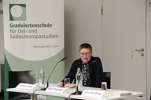 Frau Dr. Olga Shparaga sitzt hinter einem Rednerpult mit Mikrofon.