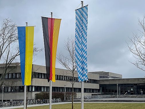 Bild der ukrainischen, deutschen und bayerischen Flagge vor der Universität Regensburg.