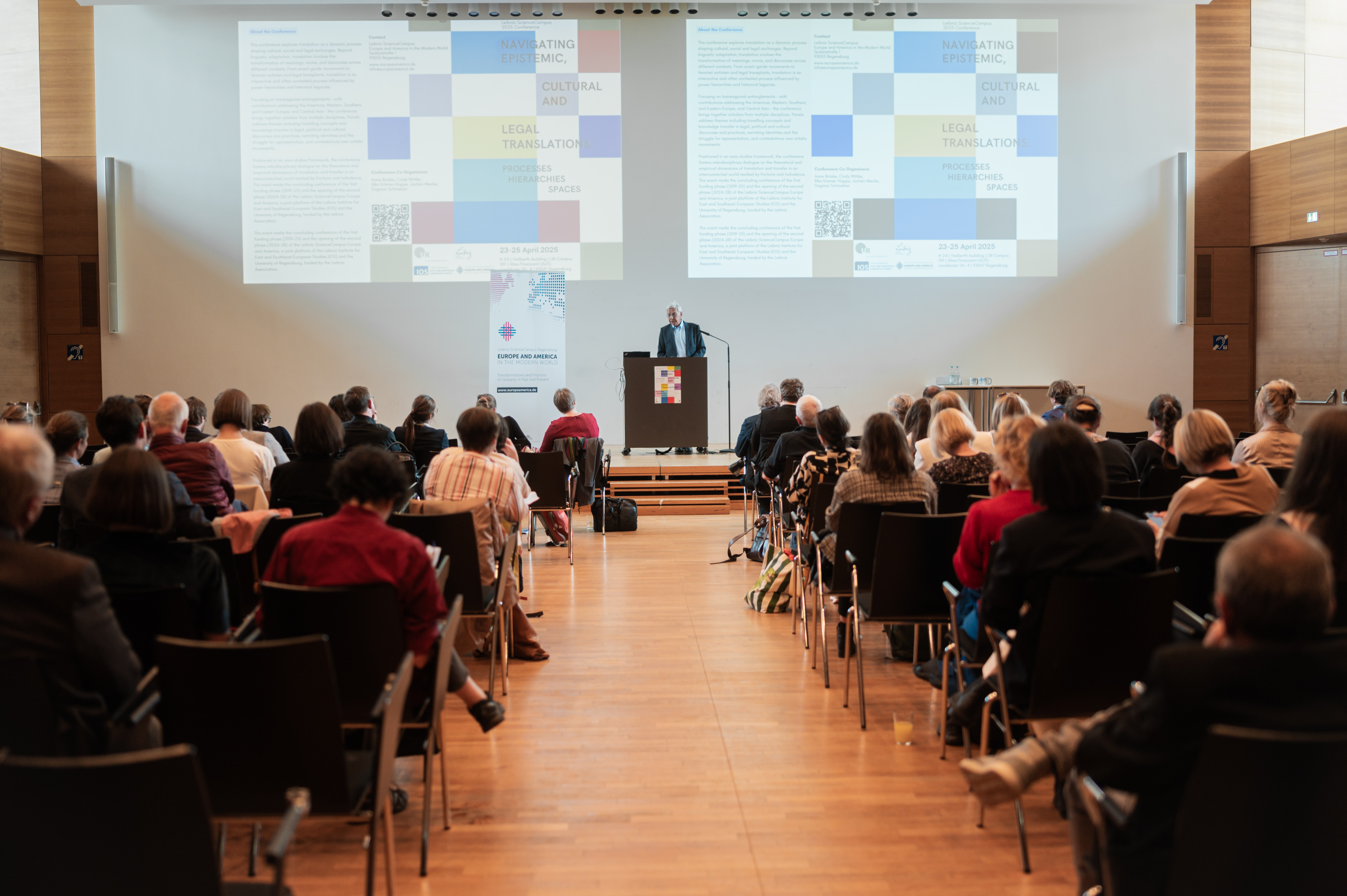 In einem Hörsaal sieht man viele Menschen von hinten sitzen, die einem Herrn beim Vortrag lauschen. (öffnet Vergrößerung des Bildes)