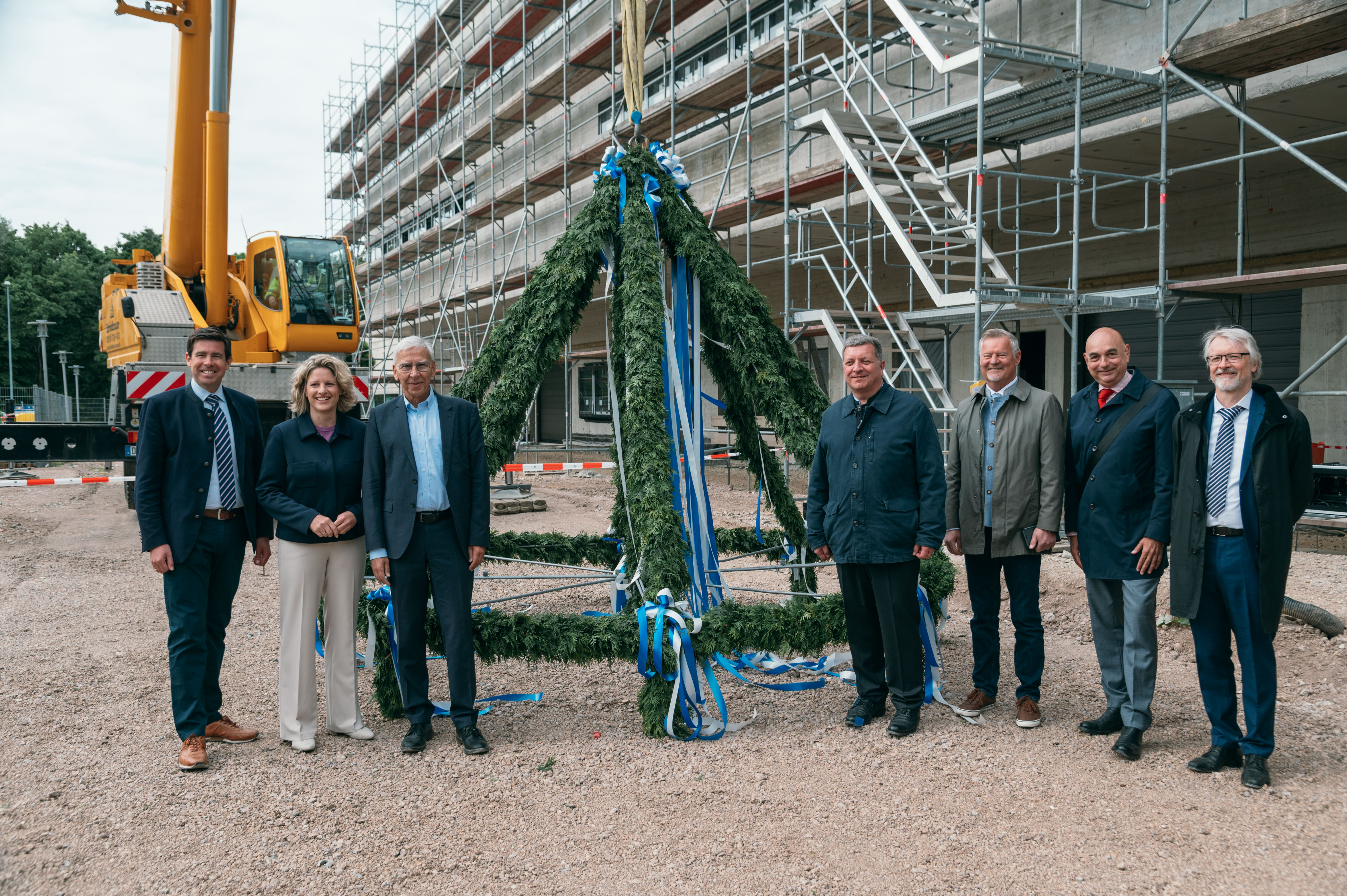Fünf Männer und eine Frau stehen an der Richtkrone und lächeln in die Kamera. Im Hintergrund der Rohbau des Werkstättengebäudes. (öffnet Vergrößerung des Bildes)