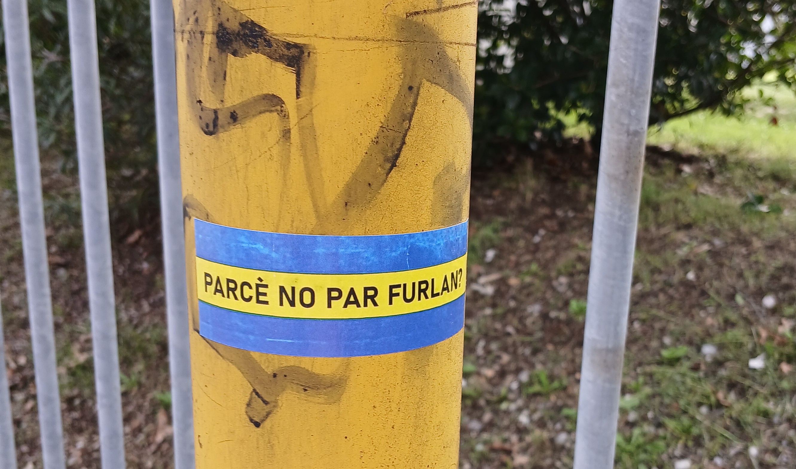 Ein Aufkleber in italienisch auf einem gelben Pfosten. (öffnet Vergrößerung des Bildes)