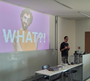 Ein Mann mittleren Alters steht vor einer Power-Point-Folie und hält einen Vortrag. 