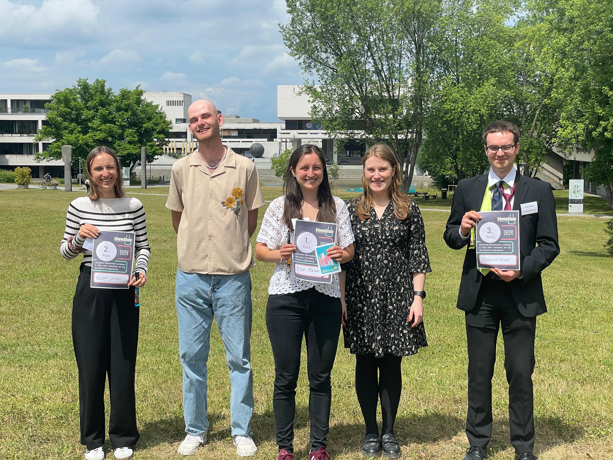 Fünf Personen schauen direkt in die Kamera und die drei Gewinner*innen zeigen ihre Urkunden. (öffnet Vergrößerung des Bildes)