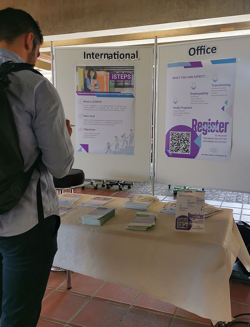 Infomessestand. Ein Student steht davor und sieht sich die Plakate an.